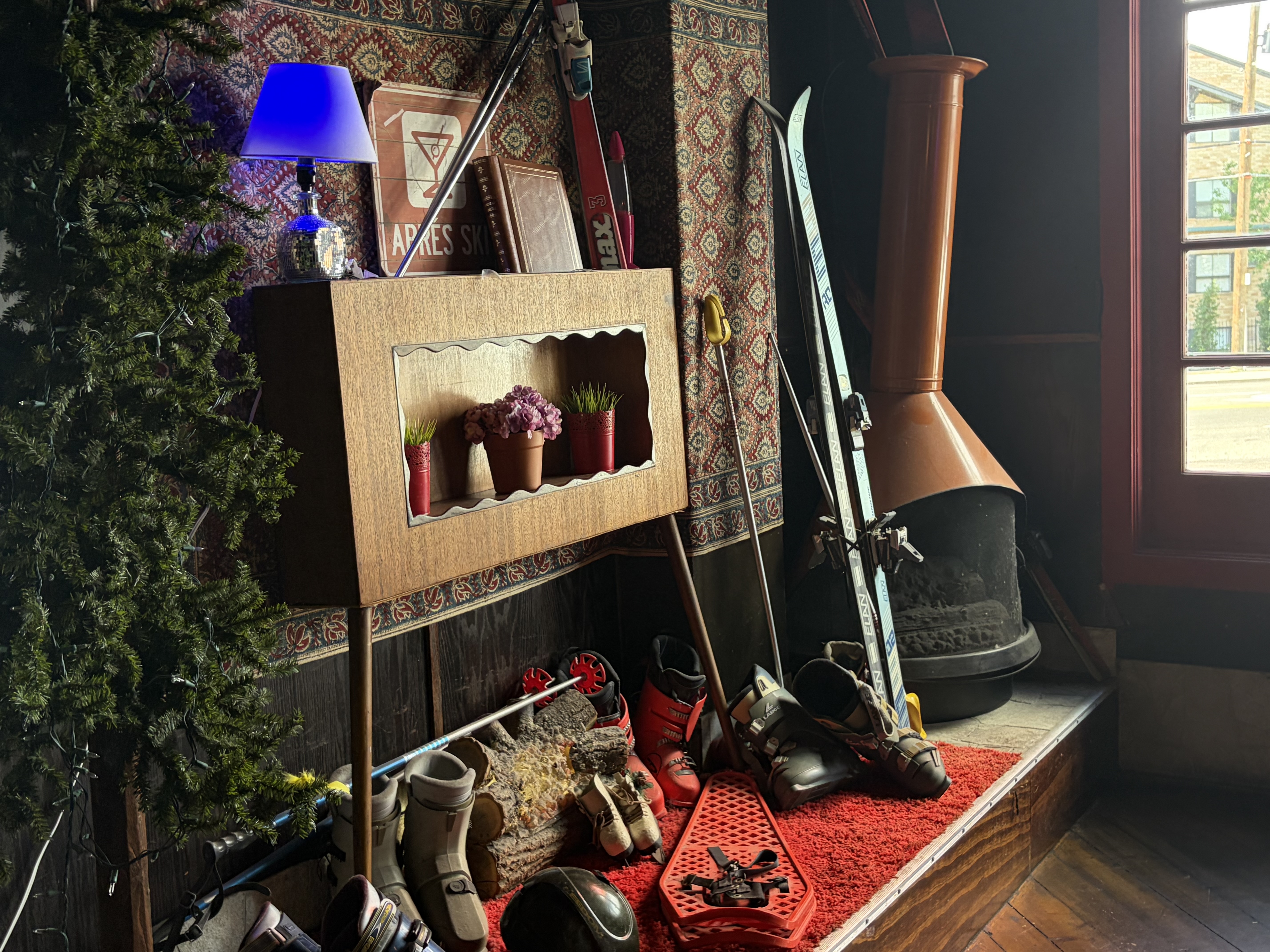 A copper cone fireplace with ski boots, poles and skis stacked around it.