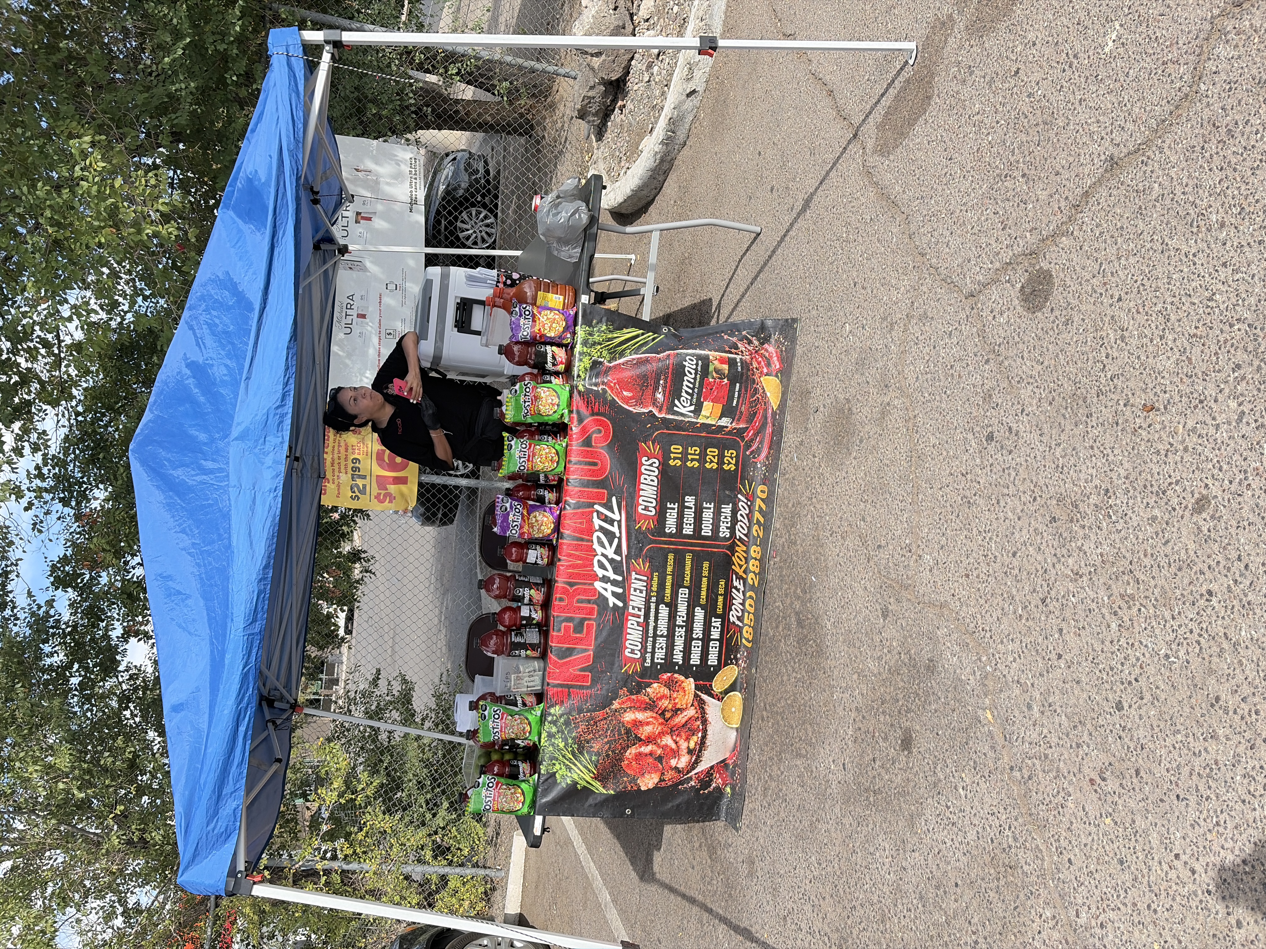 A blue canopy in the Circle K parking lot, table lined with Kermato bottles and chips, the Kermatos April banner across the front.