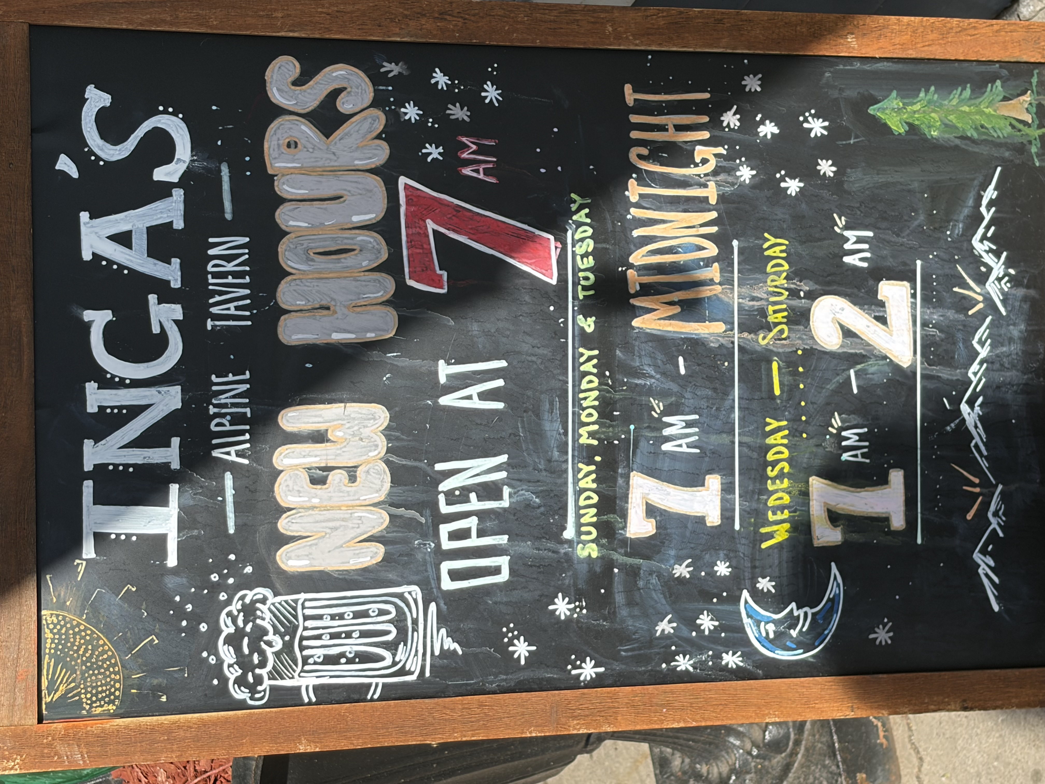 A sidewalk chalkboard reading INGA'S ALPINE TAVERN, NEW HOURS, OPEN AT 7 AM.