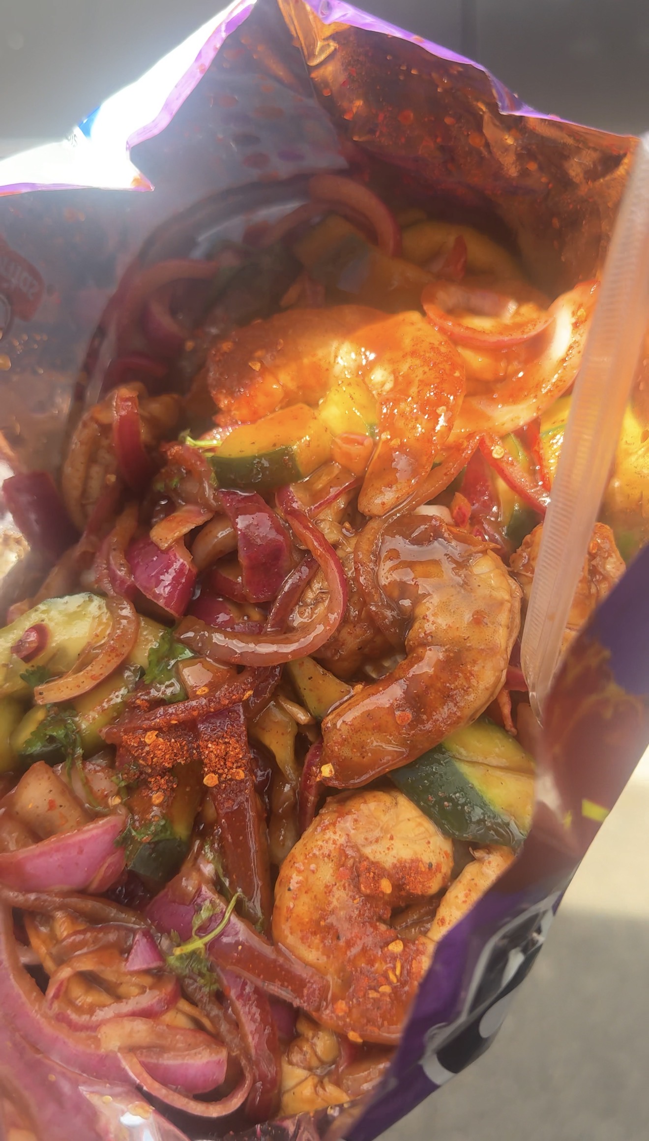 An open chip bag filled with shrimp, cucumber, red onion and chile powder.