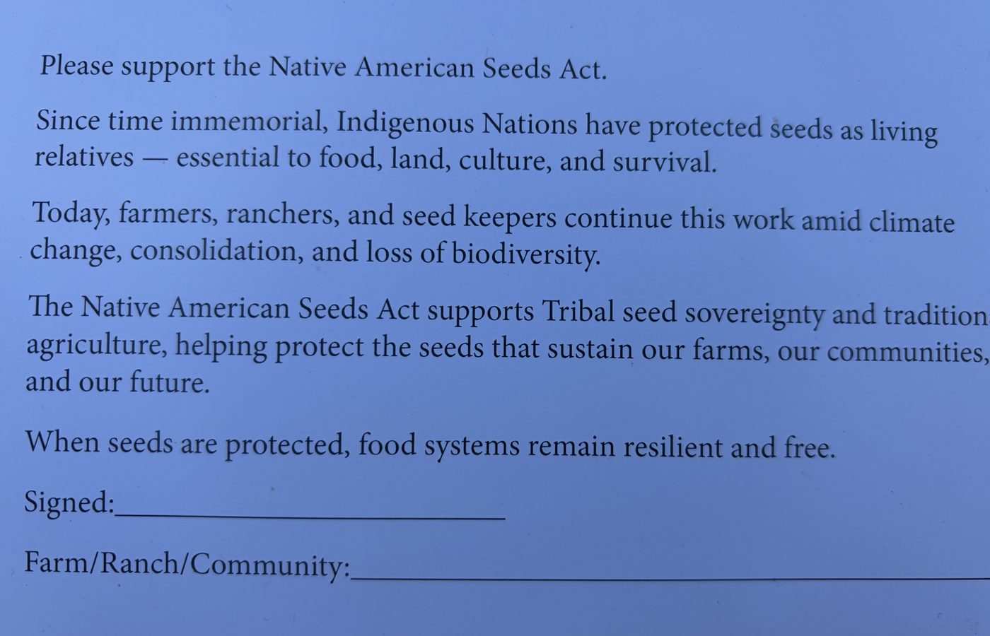 A blue petition card headed Please support the Native American Seeds Act, with lines at the bottom for a signature and a farm, ranch or community name.