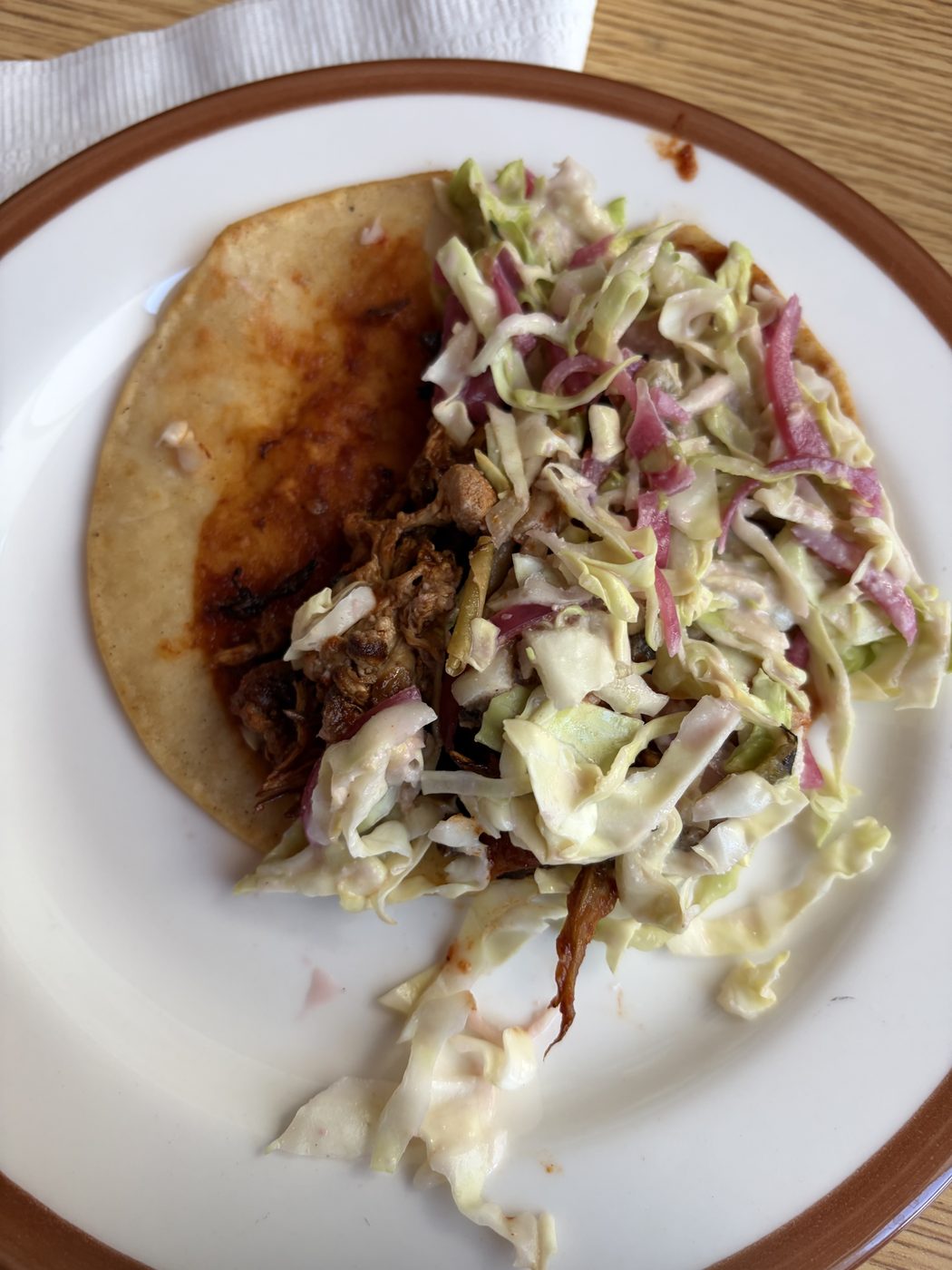 A corn tortilla taco on a white plate: housemade red chile spread across the tortilla, sautéed lion's mane and oyster mushrooms, topped with a dollop of slaw.