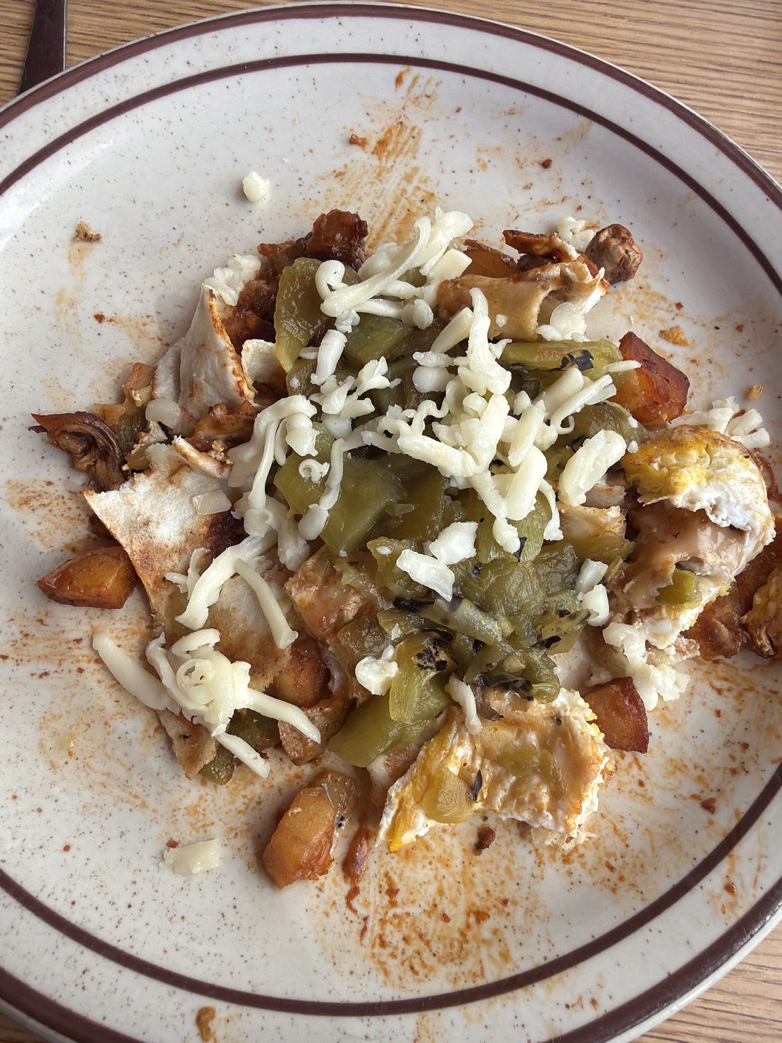 An opened burrito on a plate, its remaining filling covered in green chile and melted shredded cheese.