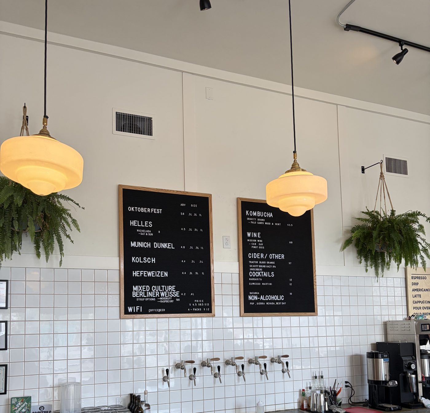 Two black letterboards under amber schoolhouse pendants listing Lasso's beer, kombucha, wine, cider, cocktails and non-alcoholic options.